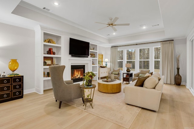 living room with a tray ceiling, crown molding, light hardwood / wood-style flooring, and ceiling fan