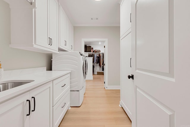 laundry room featuring cabinets, washing machine and dryer, light hardwood / wood-style flooring, and sink