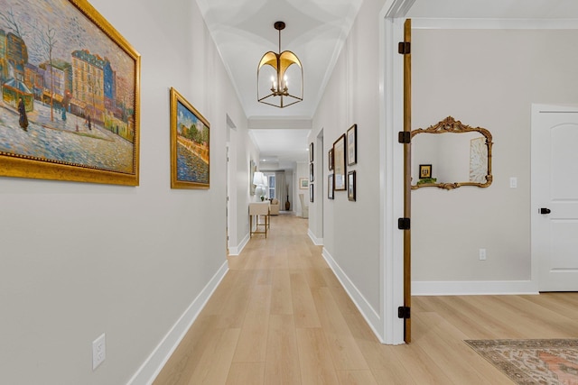 corridor with an inviting chandelier, ornamental molding, and light hardwood / wood-style flooring