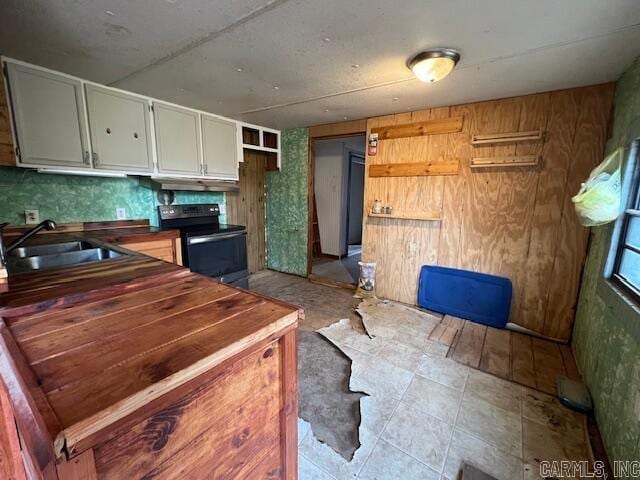 kitchen with white cabinets, sink, wooden walls, black range with electric cooktop, and butcher block counters