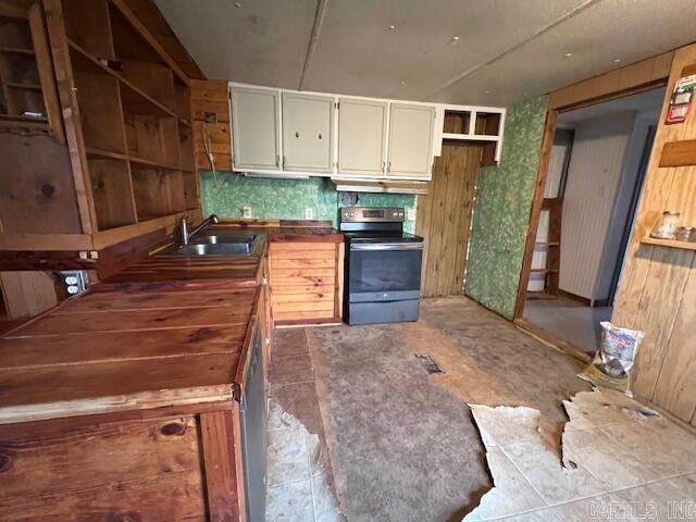 kitchen with stainless steel electric range oven, sink, backsplash, butcher block countertops, and cream cabinets