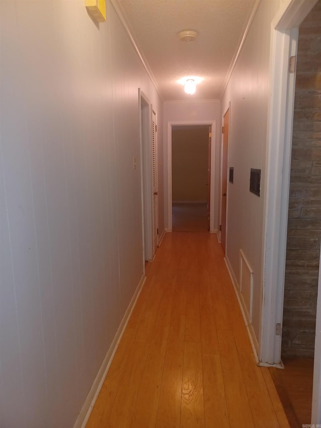 hallway with ornamental molding, light hardwood / wood-style floors, and wooden walls