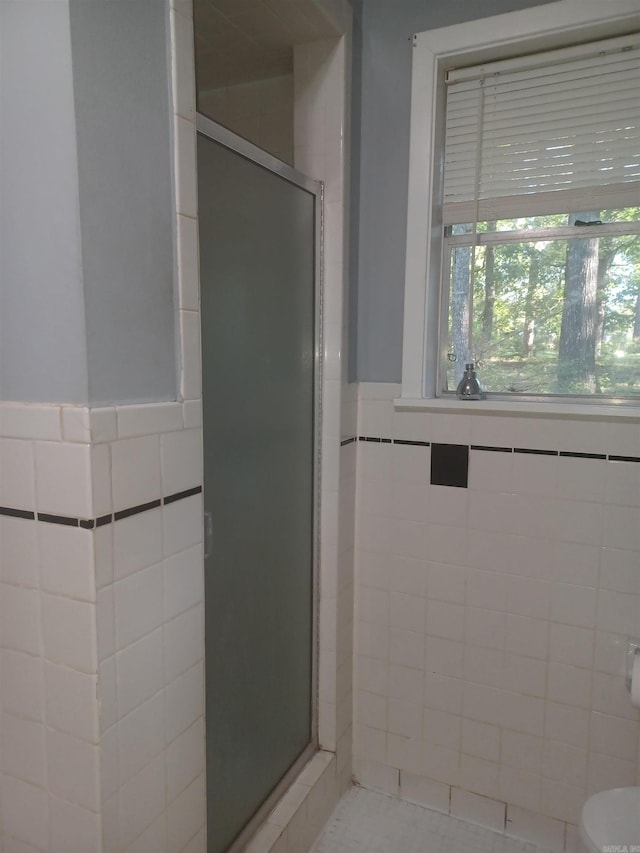 bathroom with toilet, a shower with door, and tile walls