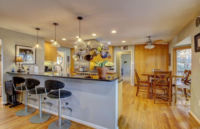 kitchen featuring ceiling fan, sink, hanging light fixtures, kitchen peninsula, and light wood-type flooring