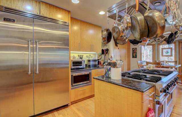 kitchen with light wood-type flooring, high end appliances, and dark stone countertops