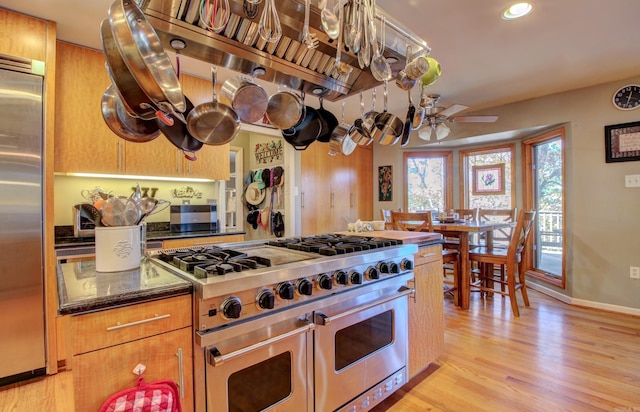 kitchen with ceiling fan, dark stone countertops, appliances with stainless steel finishes, and light hardwood / wood-style flooring