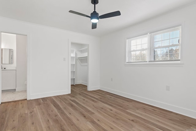 unfurnished bedroom featuring ensuite bathroom, light hardwood / wood-style flooring, ceiling fan, and a spacious closet