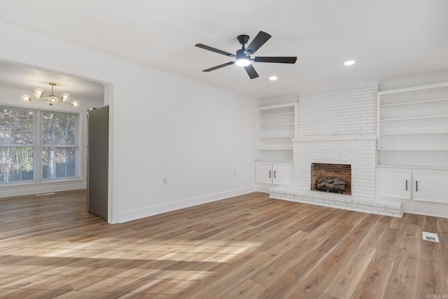 unfurnished living room with built in shelves, a fireplace, hardwood / wood-style floors, and ceiling fan with notable chandelier