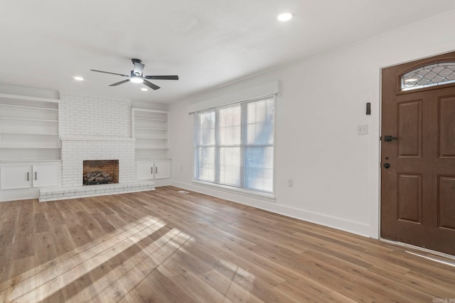 unfurnished living room featuring built in shelves, light wood-type flooring, a brick fireplace, and ceiling fan