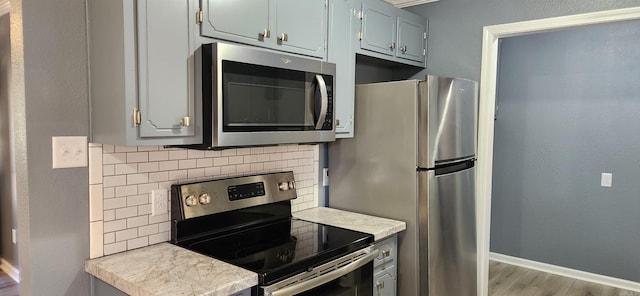 kitchen with gray cabinetry, decorative backsplash, light hardwood / wood-style floors, and appliances with stainless steel finishes