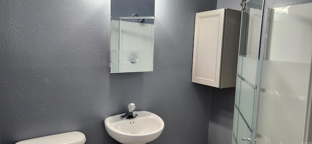 bathroom featuring sink, a shower with shower door, and toilet