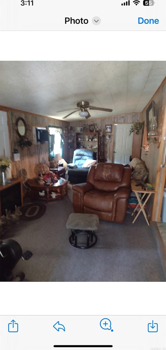 carpeted living room with ceiling fan and wood walls