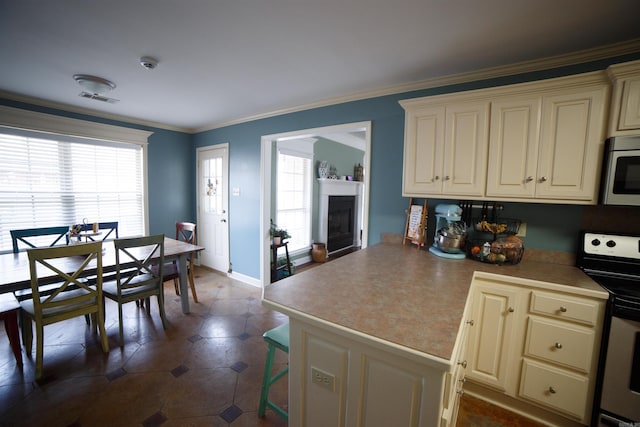 kitchen featuring stove, a wealth of natural light, ornamental molding, and cream cabinets