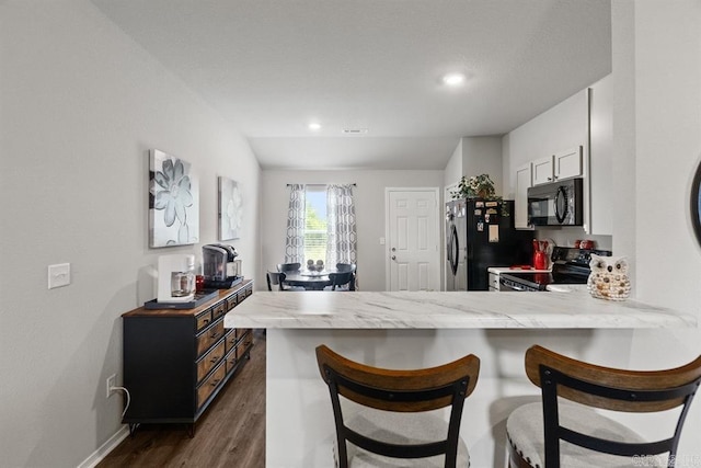 kitchen featuring kitchen peninsula, vaulted ceiling, black appliances, white cabinets, and dark hardwood / wood-style floors