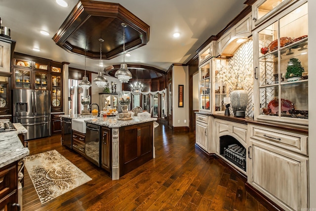 kitchen with light stone counters, an island with sink, decorative light fixtures, a tray ceiling, and appliances with stainless steel finishes