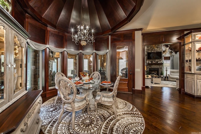 dining area with dark wood-type flooring, wooden walls, vaulted ceiling, a fireplace, and a chandelier