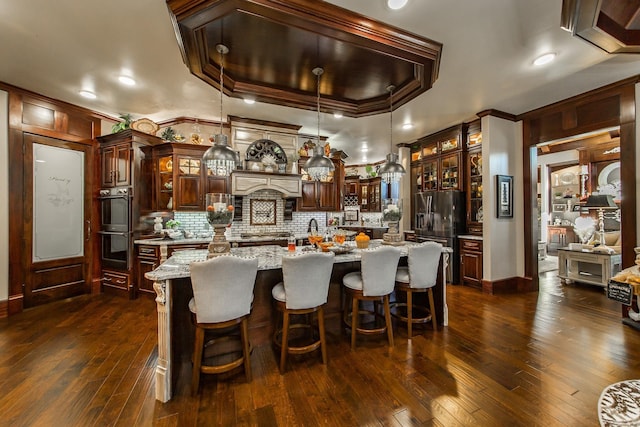 kitchen featuring light stone countertops, a raised ceiling, dark wood-type flooring, crown molding, and a kitchen island