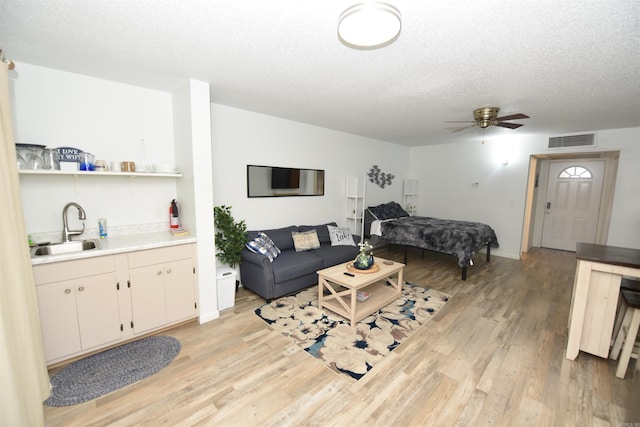 living room featuring a textured ceiling, light hardwood / wood-style floors, ceiling fan, and sink