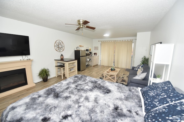 bedroom with ceiling fan, stainless steel fridge, wood-type flooring, and a textured ceiling