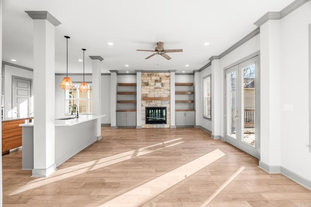 unfurnished living room featuring a stone fireplace, light wood-style flooring, recessed lighting, a sink, and crown molding