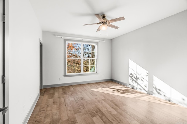 empty room with wood finished floors, a ceiling fan, and baseboards