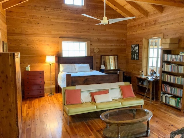 bedroom featuring beamed ceiling, light wood-type flooring, high vaulted ceiling, and wooden walls