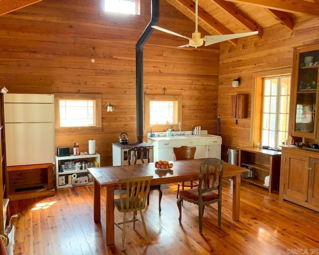 dining room featuring ceiling fan, wooden walls, light hardwood / wood-style flooring, wooden ceiling, and vaulted ceiling with beams