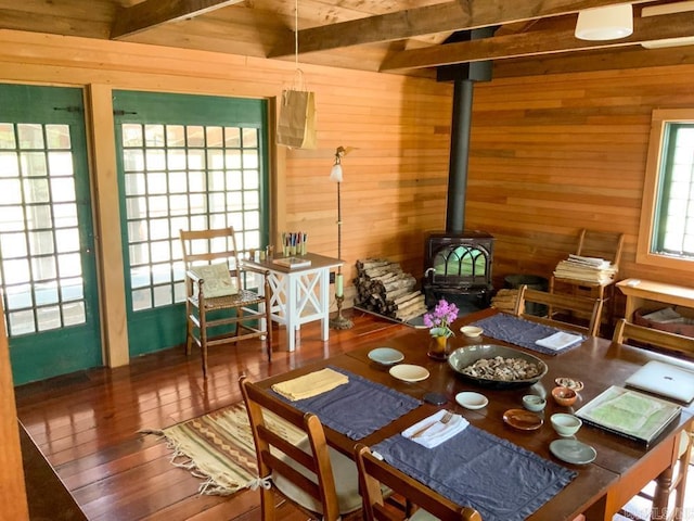 dining room featuring beam ceiling, wood-type flooring, a wood stove, and wooden walls