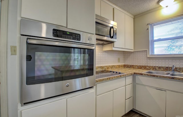 kitchen featuring sink, stainless steel appliances, backsplash, a textured ceiling, and ornamental molding