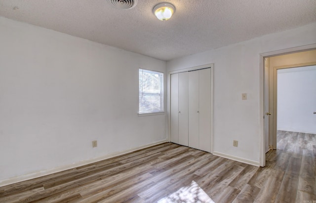 unfurnished bedroom with light wood-type flooring, a textured ceiling, and a closet