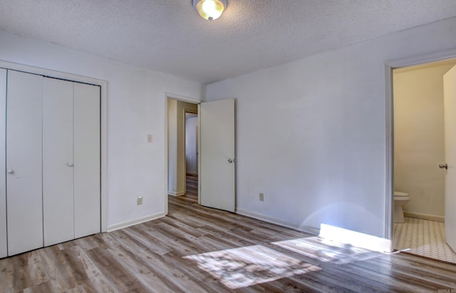 unfurnished bedroom featuring a textured ceiling, light wood-type flooring, ensuite bathroom, and a closet