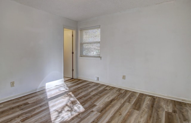 spare room featuring a textured ceiling and light hardwood / wood-style floors