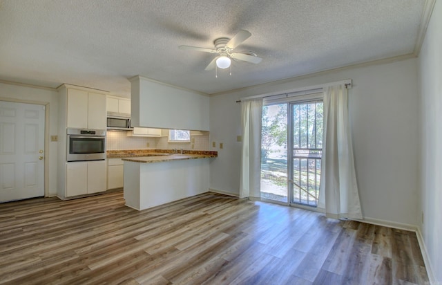 kitchen featuring white cabinets, crown molding, appliances with stainless steel finishes, light hardwood / wood-style floors, and kitchen peninsula