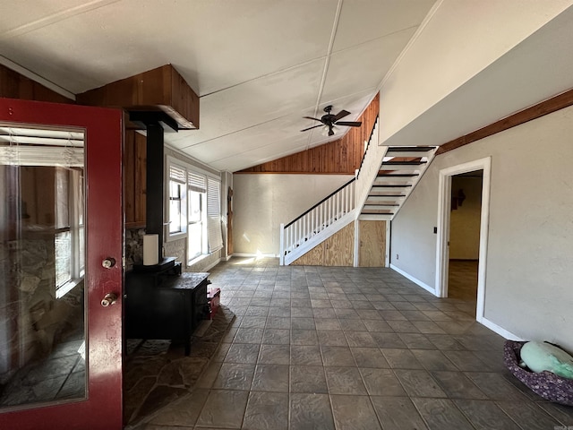 unfurnished living room featuring a wood stove, ceiling fan, wood walls, and lofted ceiling