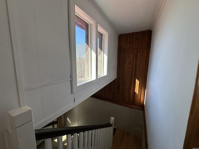 staircase with wood walls, crown molding, and a wealth of natural light