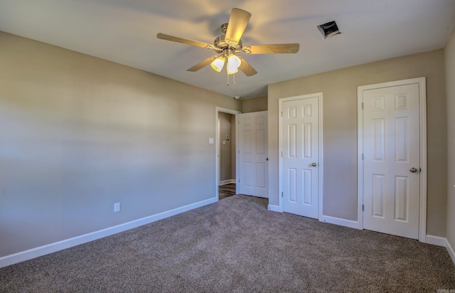 unfurnished bedroom featuring ceiling fan, dark carpet, and multiple closets