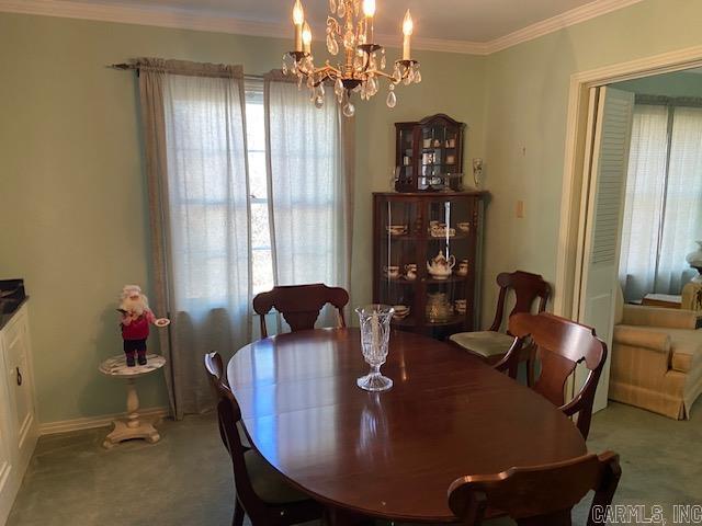 carpeted dining room featuring crown molding and an inviting chandelier