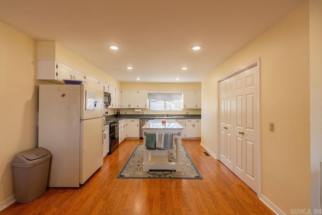 kitchen with appliances with stainless steel finishes, a kitchen island, sink, light hardwood / wood-style flooring, and white cabinetry