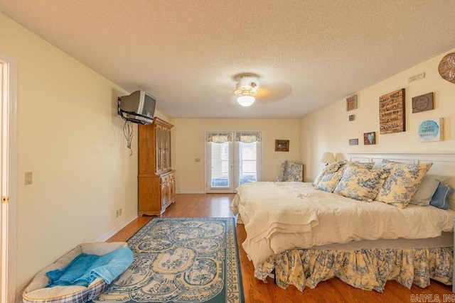 bedroom with access to exterior, ceiling fan, wood-type flooring, and a textured ceiling