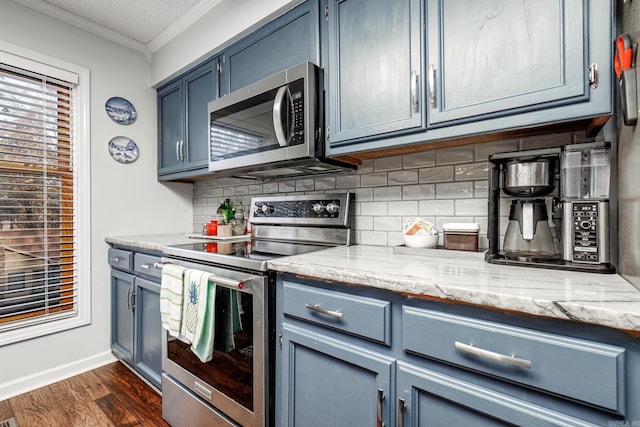 kitchen featuring dark wood-type flooring, blue cabinets, crown molding, appliances with stainless steel finishes, and tasteful backsplash