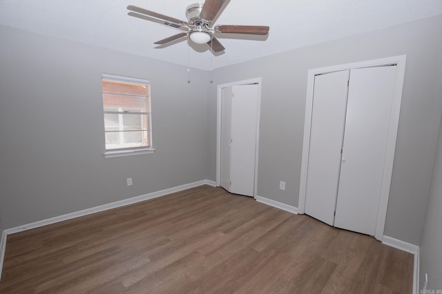 unfurnished bedroom featuring ceiling fan, wood-type flooring, and two closets