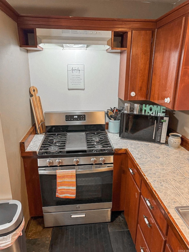 kitchen with dark tile patterned flooring, range hood, tile counters, and stainless steel range with gas stovetop