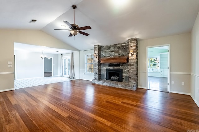 unfurnished living room with hardwood / wood-style flooring, ceiling fan with notable chandelier, a brick fireplace, and vaulted ceiling