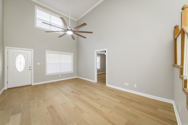 entrance foyer with crown molding, a towering ceiling, a healthy amount of sunlight, and light wood-type flooring