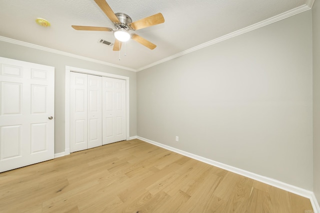 unfurnished bedroom featuring light wood-type flooring, a textured ceiling, ceiling fan, crown molding, and a closet