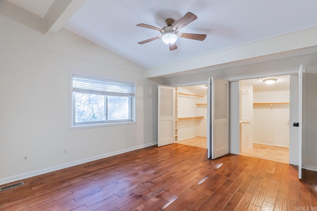 unfurnished bedroom with hardwood / wood-style floors, ceiling fan, lofted ceiling with beams, and a walk in closet