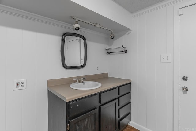 bathroom with a textured ceiling, vanity, ornamental molding, and wood walls