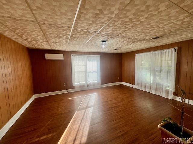 spare room with an AC wall unit, dark wood-type flooring, and wooden walls