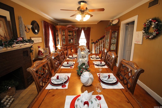 tiled dining area featuring ceiling fan, crown molding, and a brick fireplace