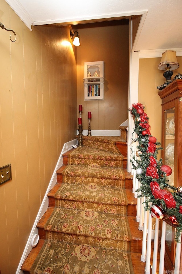staircase with hardwood / wood-style floors, ornamental molding, and wooden walls